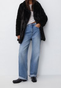 Zwarte nepbontjas, lichtgrijze top, oversized blauwe denim jeans met rafelige zoom, en zwarte enkellaarsjes. Eenvoudige, casual outfit.