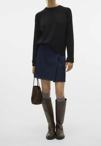 Czarna bluza, dżinsowa spódnica o kroju zawijanym, brązowe skórzane kozaki do kolan i szare skarpetki. Brązowa torba trzymana w ręku. Prosty, casualowy strój.