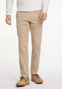 Beige cotton chinos featuring a straight leg cut, side pockets, and a smooth texture, paired with light-colored suede shoes.