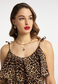 Halenka s leopardím potiskem, která má volánové vrstvy, tenké ramínka s mašlemi, doplněná o vrstvené zlaté náhrdelníky a kruhové náušnice.