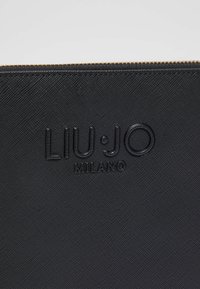 Pochette en cuir noir texturé avec logo embossé "LIU·JO MILANO" et détail de fermeture éclair dorée. Forme rectangulaire compacte, design minimaliste.