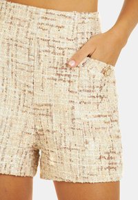 Shorts en tweed beige clair avec un motif texturé. Dotés d'une poche latérale et d'un bouton décoratif, mettant en avant un design structuré.
