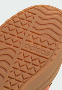 Potplat Adidasove cipele ima teksturiranu gumenu površinu u narančastoj boji s cik-cak uzorkom i brendirano ime u središtu.