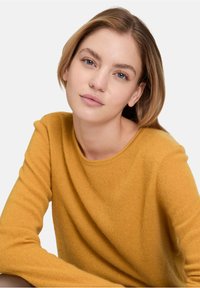 Musztardowy żółty sweter dzianinowy z okrągłym dekoltem i długimi rękawami, charakteryzujący się miękką fakturą i luźnym krojem.