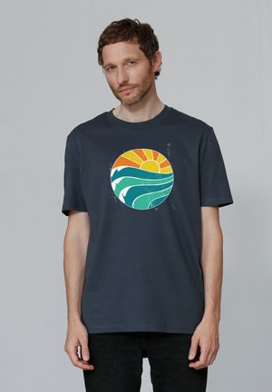 T-shirt en coton bleu marine avec un motif rond représentant un soleil et des vagues en orange, jaune et vert. Manches courtes et coupe décontractée.