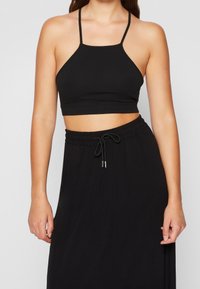 Černý zkrácený top bez rukávů vyrobený z hladkého materiálu s tenkými řemeny a rovým lemem, doplněný černou sukní se šňůrkou.