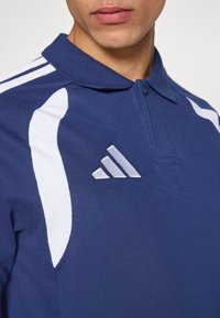 Πόλο μπλουζάκι σε ναυτικό μπλε χρώμα με λευκές λεπτομέρειες, κατασκευασμένο από υφασμάτινη υφή. Διαθέτει γιακά με κουμπιά και κεντημένο λογότυπο στο αριστερό στήθος.