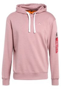 Sudadera con capucha de tela rosa claro con cordones blancos. Presenta un parche de logo en la parte delantera y un bolsillo con cremallera en la manga con una etiqueta roja.