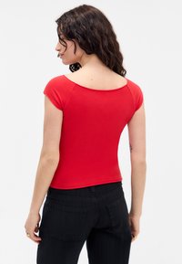 Top rojo de manga corta con un amplio escote en forma de barco, diseño ajustado y tejido suave. Combinado con pantalones negros texturizados, que muestran un estilo minimalista.
