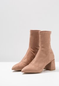Bottines en daim couleur nude avec un bout pointu et un talon carré, présentant des détails cousus et une tige ajustée.