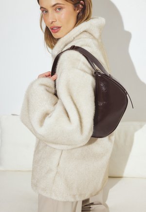 Kreemjas, pehme jakk üle suurte varrukatega; tumepruunast nahast käekott, millel on kõver kuju ja kitsas rihm, hoituna ühe õla peal.