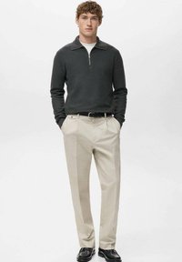 Pull gris à col zippé avec manches longues, associé à un pantalon crème fuselé et des chaussures noires. Design sobre, texture douce et coupe ajustée.