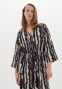 Robe longue à col en V crème avec des rayures abstraites noires, dotée de manches trois-quarts et d'une taille à cordon pour un ajustement.