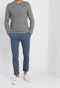 Pull en maille grise, pantalon bleu avec revers roulés, et baskets blanches. La tenue présente une coupe décontractée et des textures douces.