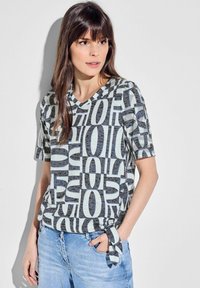 V-hals, kortærmet t-shirt i lys grå med sorte tekstmønstre. Har en knyttet detalje i taljen og en afslappet pasform.