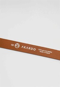 Hnedý kožený remienok z pravej kože s štruktúrovaným povrchom. Obsahuje logo AKARDO a text v bielej farbe, ktorý uvádza materiál a pôvod: Vyrobené v Poľsku.
