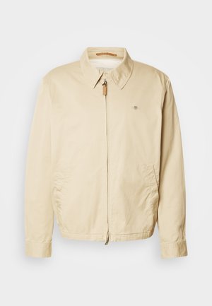 Beige Reißverschlussjacke mit Kragen, zwei seitlichen Taschen, langen Ärmeln und einem kleinen gestickten Logo auf der Brust.