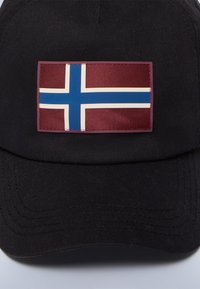 Svart keps med en rektangulär yta som har Islands flagga. Flaggan har en vinröd bakgrund, vit kors och blå detaljer.