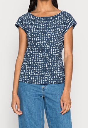 Top blu navy con un motivo astratto bianco, maniche corte e scollatura ampia. Abbinato a jeans a gamba larga blu chiaro.