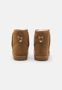 Bottines en daim marron avec doublure douce, dotées d'un col rembourré, d'étiquettes logo et d'une semelle en caoutchouc plate pour le confort et le soutien.