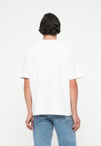 Valge lühikeste varrukatega T-särk sirge lõike, ümmarguse kaelusega ja pehme puuvilla tekstuuriga, koos helesiniste denimist teksadega.