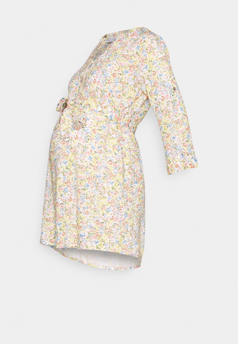 Vestido de maternidade floral em amarelo pastel, com mangas 3/4, um laço na cintura e um corte descontraído que se adapta a uma barriga em crescimento.
