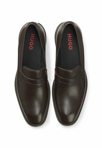 Braune Slipper aus Leder mit glatter Oberfläche, versehen mit einem geschwungenen Vorderdetail und einem roten "HUGO"-Logo auf der Innensohle.