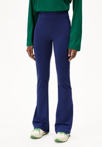 Navyblauwe flared broek met een stretchy, hoge tailleband. Stijlvol gecombineerd met een losse groene lange mouwen shirt en lichtgekleurde sneakers.