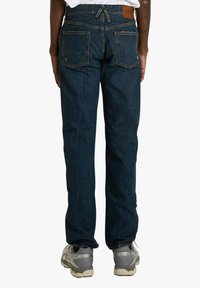 Jeans in denim blu scuro con taglio a gamba dritta, con due tasche posteriori, cuciture visibili e una targhetta in pelle sulla vita.