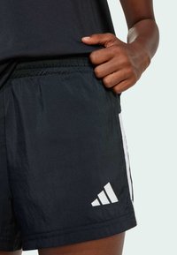 Black athletic shorts made of smooth, lightweight material, featuring a white logo and contrasting side stripes. Elastic waist for comfort.