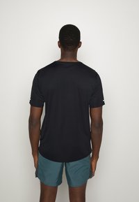 Svart, kortärmad atletisk t-shirt med rund hals, visad bakifrån, i kombination med turkosa shorts. Slät, fuktavledande tyg.