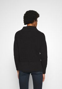 Suéter negro acanalado con cuello alto, diseño ajustado, mangas largas y tejido texturizado. El dobladillo inferior es ligeramente acampanado.