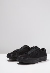 Zapatillas de ante negras con detalles texturizados, cordones planos negros y un logo de estrella en el lateral. Cuenta con una suela de goma y un diseño de punta redondeada.