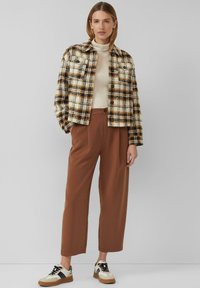 Kurtka wełniana w kratę w kolorach kremowym, brązowym i czarnym; beżowy golf; brązowe spodnie o szerokich nogawkach; białe i czarne sneakersy.