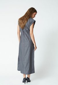 Rochie gri până la genunchi, cu mâneci scurte, având un model subtil, fante laterale și o textură fină. Puritată cu pantofi cu toc înalt negri.