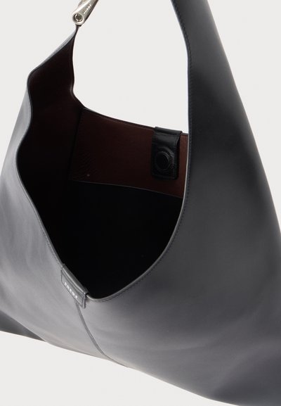 Μαύρη δερμάτινη τσάντα ώμου με φαρδιά λωρίδα και κλεισίματα με μαγνητικό κουμπί, που δείχνει κενή καφέ εσωτερική επένδυση.