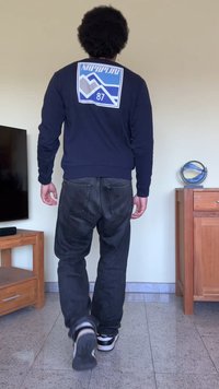 Sweatshirt azul da NapaPura com gráfico de montanha branca e texto nas costas, combinado com jeans escuros e sapatos pretos. Mobiliário de madeira ao fundo.