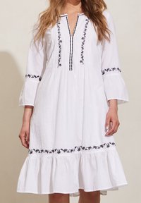White cotton dress with black floral embroidery along the neckline and sleeves. Features a flared skirt and a modest V-neck design.