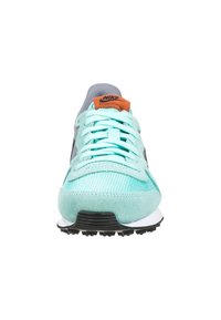 Zapatillas Nike con parte superior de malla y ante en verde menta, acentos grises, suela negra y logotipo naranja en la lengüeta. Cuenta con cordones planos.