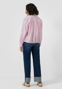 Light pink striped shirt with a gathered back and long sleeves, paired with dark blue denim jeans and light-colored shoes.