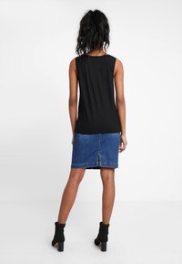 Svart ärmlös topp i kombination med en jeanspennkjol, med en slits bak och bärs med svarta ankelboots. Slät tygtextur.