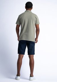 Polo verde oliva con maniche corte, colletto a costine e dettagli verdi, abbinato a pantaloni corti blu navy e sneakers bianche.