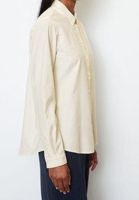 Camisa de manga larga color beige claro con un cierre de botones en la parte delantera, cuello puntiagudo y un corte relajado, fabricada en una suave mezcla de algodón.