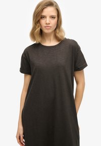 T-shirt noir surdimensionné en tissu léger. Doté d'un col rond et de manches courtes retroussées, avec une coupe décontractée et ample.