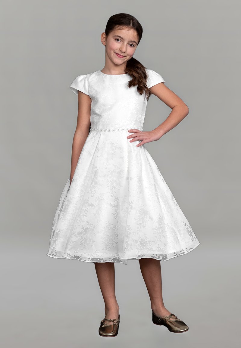 Weißes Kleid mit floralem Muster, kurzen Cap-Ärmeln, einem taillierten Oberteil und einem ausgestellten, knielangen Rock; kombiniert mit braunen flachen Schuhen.