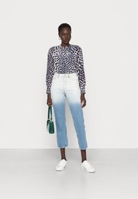 Blusa de mangas longas com um padrão de leopardo em azul-marinho e branco, combinada com jeans de cintura alta que apresentam um efeito ombre do claro ao escuro.