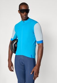 Maillot de cyclisme à manches courtes en bleu vif avec fermeture éclair en front et panneaux en bleu clair texturés, associé à un short de cyclisme rembourré bleu foncé.