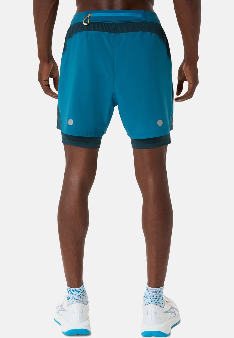 Shorts de sport bleus avec une taille à cordon de serrage, une poche arrière et des accents réfléchissants. Matériau léger, associés à des chaussures de course blanches et des chaussettes à motifs.