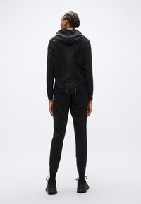 Μαύρο αθλητικό φούτερ με υφή, με ιδιαίτερο σχέδιο στην πλάτη, κουκούλα και κίτρινα στοιχεία. Συνδυάζεται με αντίστοιχο παντελόνι.