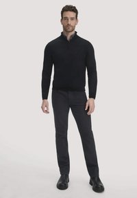 Schwarzer Zip-Kragen-Pullover mit langen Ärmeln, kombiniert mit dunkelgrauen Hosen und schwarzen Schuhen. Das Outfit hat eine figurbetonte Passform und eine glatte Textur.